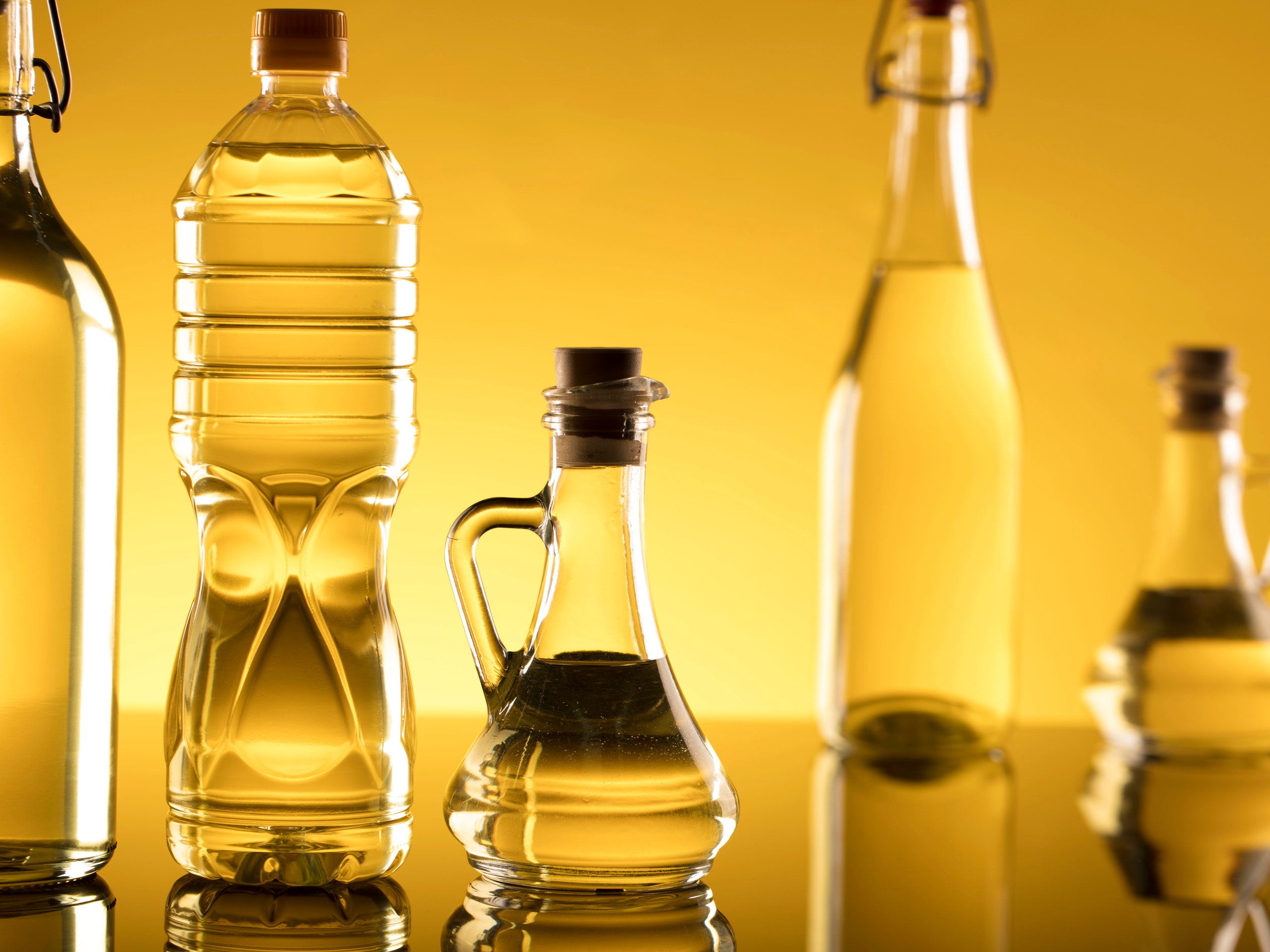 bottles of seed oils for cooking with glass reflection against a yellow background