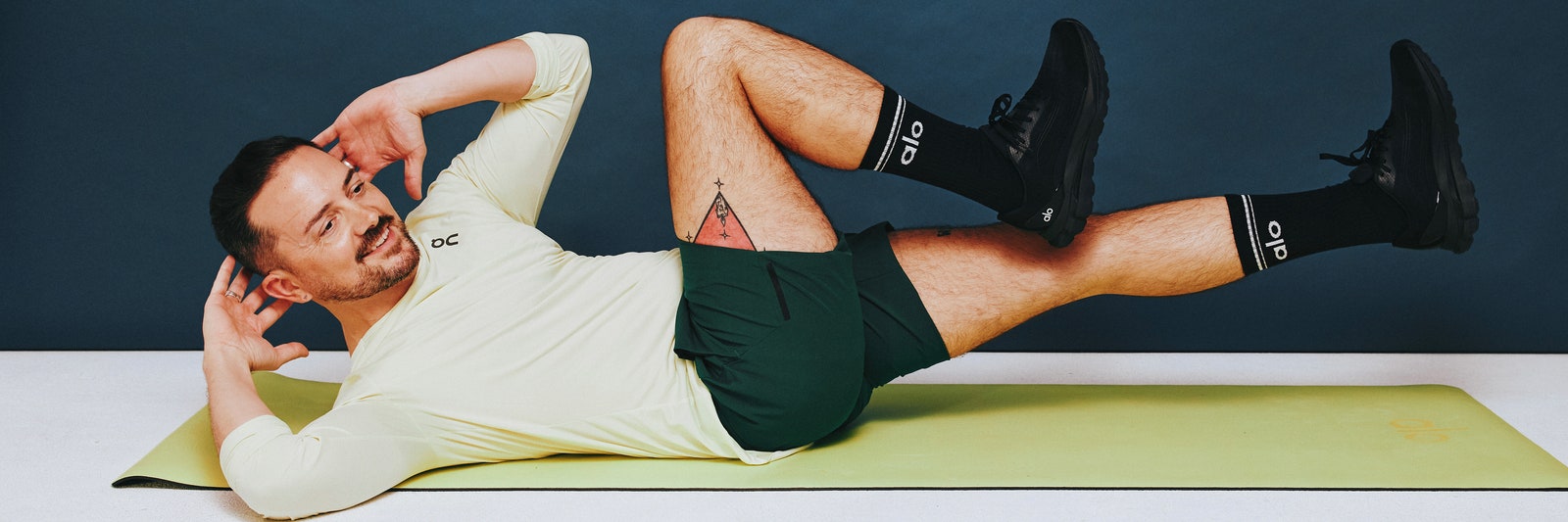 Fitness model performing a bicycle crunch on a green mat